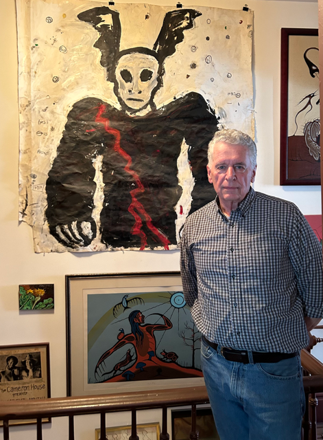 Herb Tookey in front of a large scale "Bunny-Man" by John Scott, above a small flower painting by Lorne Wagman and a print by indigenous artist Carl Ray.