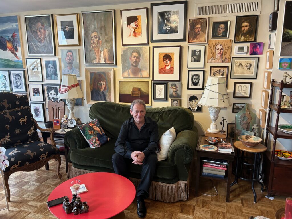 Flavio Belli sitting in his living room in front of his wall of strategically placed portraits